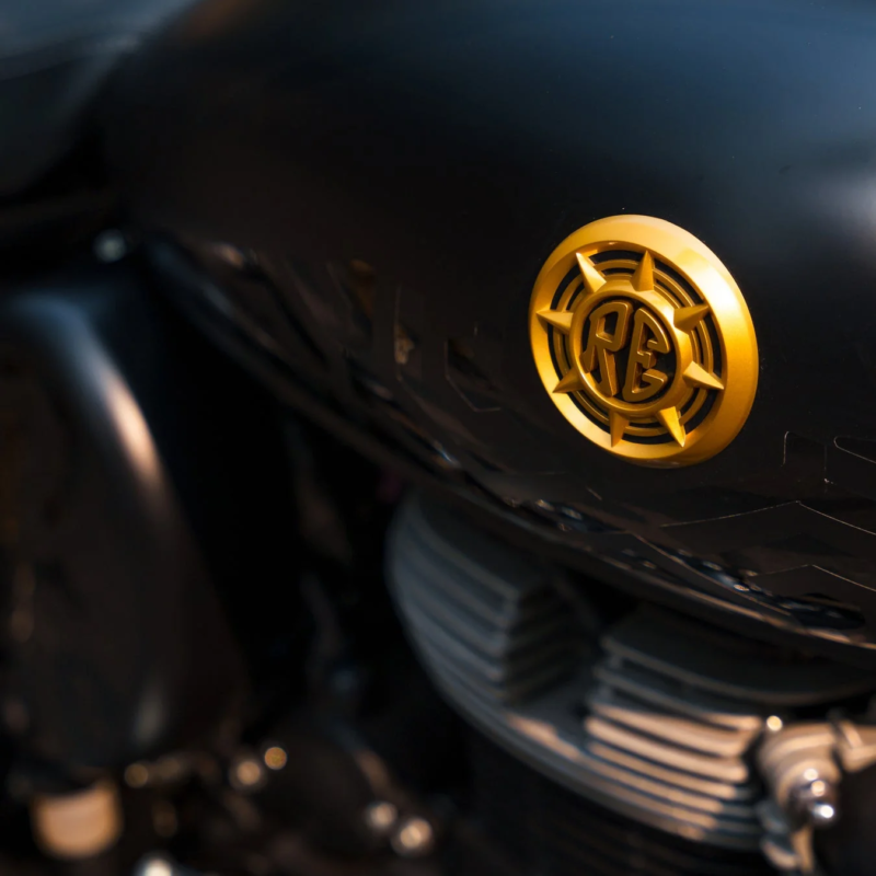 黒いバイクの燃料タンクに取り付けられた、金色に輝く「RE」ロゴのエンブレム